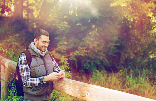 travel, tourism, hike, technology and people concept - happy man with backpack and smartphone outdoors