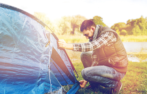 travel, tourism and hike concept - happy male traveler setting tent up outdoors