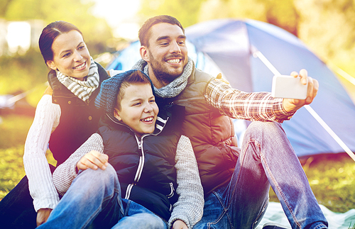 hike, travel and technology concept - happy family with smartphone taking selfie at campsite