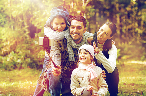 travel, tourism, hike, technology and people concept - happy family taking picture with smartphone selfie stick in woods