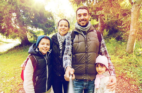 technology, travel, tourism, hike and people concept - happy family with backpacks taking picture by selfie stick and hiking