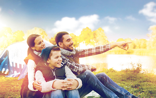 camping, tourism, hike and people concept - happy family over tent at camp site pointing finger to something