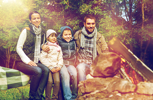 travel, hike and tourism concept - happy family sitting on bench and talking at camp near campfire in woods