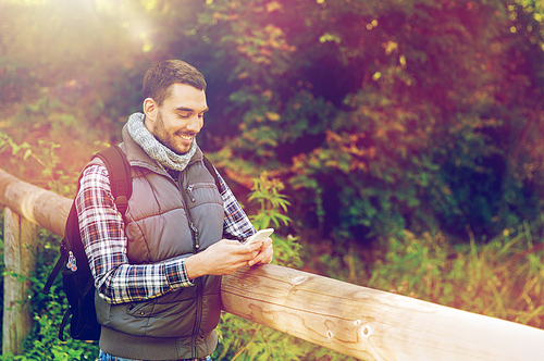 travel, tourism, hike, technology and people concept - happy man with backpack and smartphone texting message outdoors