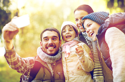 travel, tourism, hike, technology and people concept - happy family with backpacks taking selfie by smartphone outdoors