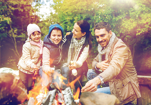 camping, hike and people concept - happy family roasting marshmallow over campfire