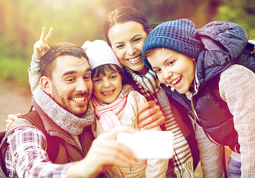 travel, tourism, hike, technology and people concept - happy family with backpacks taking selfie by smartphone in woods