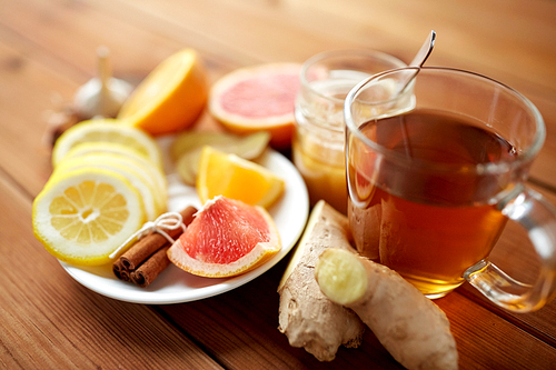 health, traditional medicine, folk remedy and ethnoscience concept - cup of ginger tea with honey, citrus and cinnamon on wooden background