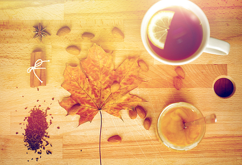 autumn and ethnoscience concept - cup of lemon tea and honey on wooden board with maple leaf and almond