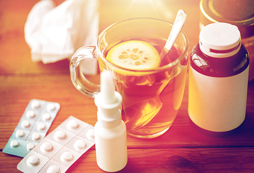 healthcare, medicine and treatment concept - cup of tea, drugs, honey and paper tissue on wooden table