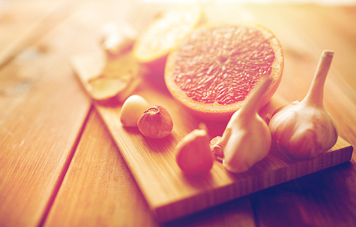 traditional medicine, cooking, food and ethnoscience concept - garlic and grapefruit on wooden board