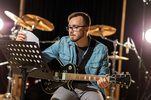 music, people, musical instruments and entertainment concept - male guitarist playing electric guitar with stand at studio rehearsal