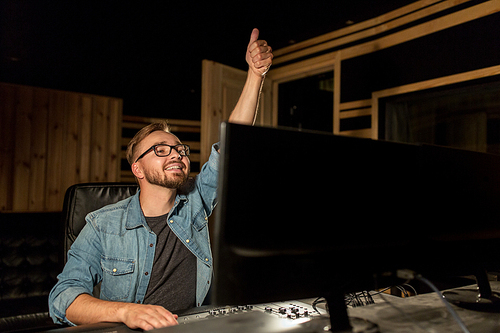 music, technology, gesture and people concept - happy man at mixing console in sound recording studio showing thumbs up
