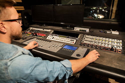 music, technology, people and equipment concept - man at mixing console in sound recording studio