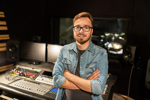 music, technology, people and equipment concept - happy smiling man at mixing console in sound recording studio