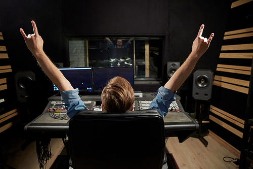 music, technology, people and equipment concept - happy man at mixing console in sound recording studio showing rock gesture