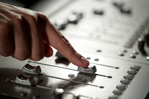 music, technology, people and equipment concept - hand using mixing console in sound recording studio