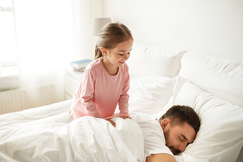 people, family and morning concept - happy little girl waking her sleeping father up in bed at home