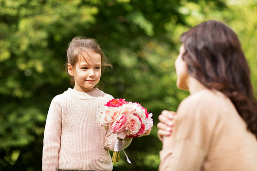 family, holidays and people concept - happy little girl giving flowers to mother in summer park