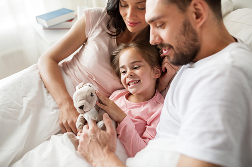 people, family and morning concept - happy child with toy rabbit and parents in bed at home