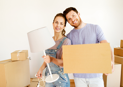 mortgage, people and real estate concept - happy couple with boxes and lamp moving to new home