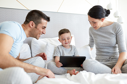 people, family and technology concept - happy mother, father and little boy with tablet pc computer in bed at home or hotel room