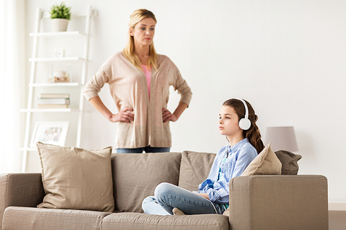 people, problem and family concept - girl with earphones sitting on sofa and angry mother at home
