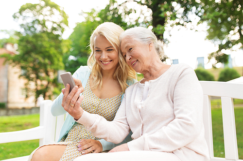 family, generation and people concept - happy smiling young daughter and senior mother with smartphone sitting on park bench