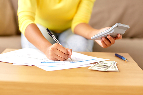 business, finances and people concept - woman with money, papers and calculator at home
