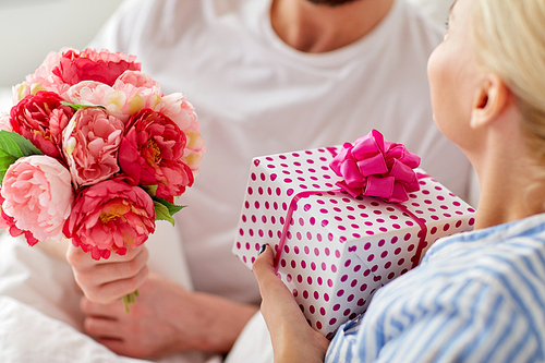holidays, birthday, valentines day, romance and people concept - close up of happy couple with gift box and flowers in bed at home