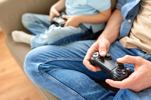 family, fatherhood and people concept - close up of father and little son with gamepads playing video game at home