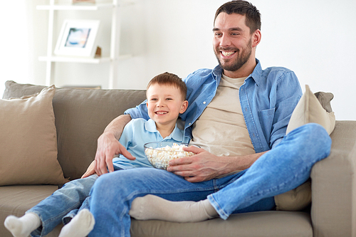 family, childhood, fatherhood, technology and people concept - happy father and little son with popcorn watching tv at home
