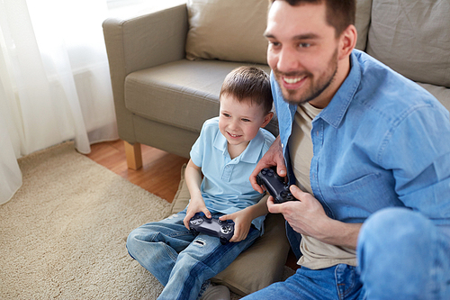family, fatherhood and people concept - happy father and little son with gamepads playing video game at home