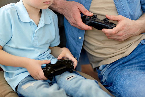 family, fatherhood and people concept - close up of father and little son with gamepads playing video game at home