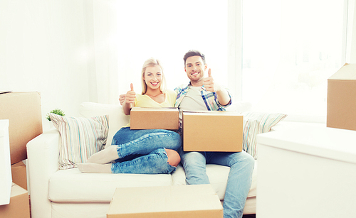 moving, people, repair and real estate concept - happy couple with big cardboard boxes showing thumbs up on sofa at new home