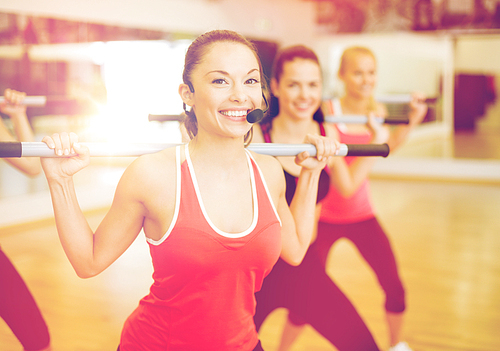 fitness, sport, training, gym and lifestyle concept - smiling trainer in front of the group of people working out with barbells in the gym