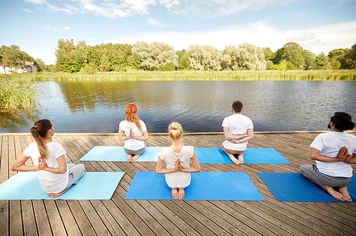 fitness, sport, yoga and healthy lifestyle concept - group of people exercising in reverse prayer pose on river or lake berth