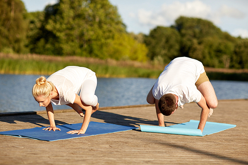 fitness, sport, yoga, people and healthy lifestyle concept - couple making side crow pose on mat on river or lake berth