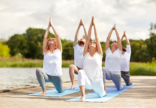 fitness, sport, yoga and healthy lifestyle concept - group of people making low lunge or crescent pose on river berth
