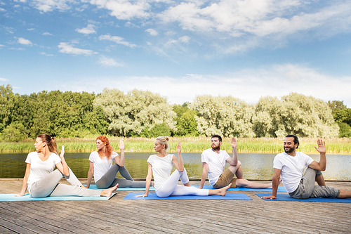 yoga, fitness, sport, and healthy lifestyle concept - group of people sitting in half lord of the fishes pose on mat outdoors on river or lake berth