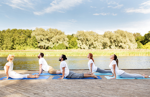 yoga, fitness, sport, and healthy lifestyle concept - group of people making upward facing dog or cobra pose on river or lake berth
