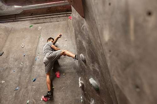fitness, extreme sport, bouldering, people and healthy lifestyle concept - young man exercising at indoor climbing gym wall