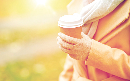 season, hot drinks and people concept - close up of woman with coffee or tea disposable paper cup in autumn park