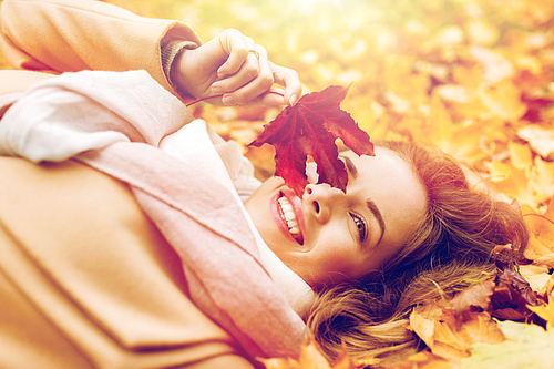 season and people concept - beautiful young woman with autumn maple leaf lying on ground