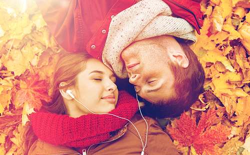 love, relationship, season, family and people concept - close up of happy couple with earphones listening to music and lying on autumn leaves