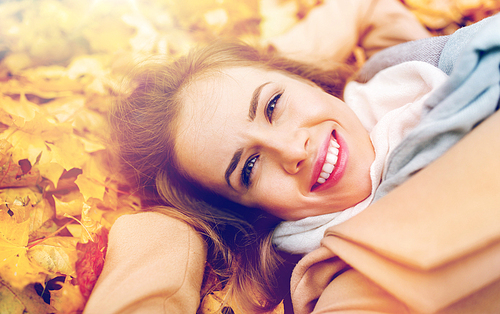 season and people concept - beautiful young woman lying on ground and autumn leaves