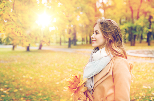 season and people concept - beautiful young woman with maple leaves walking in autumn park