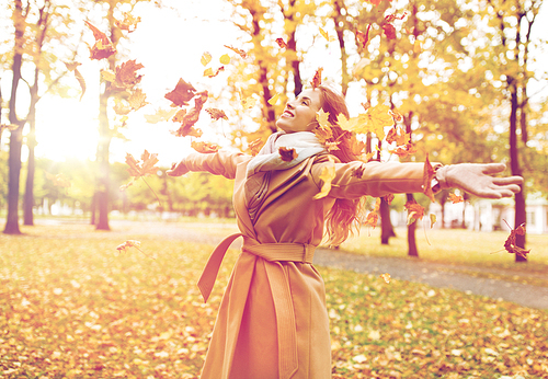 season and people concept - beautiful happy young woman having fun with leaves in autumn park