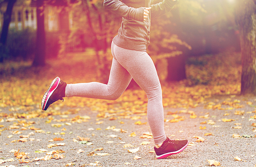 fitness, sport, people, wear and healthy lifestyle concept - close up of young woman running in autumn park