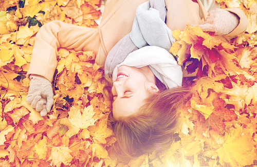 season and people concept - beautiful young woman with autumn maple leaves lying on ground